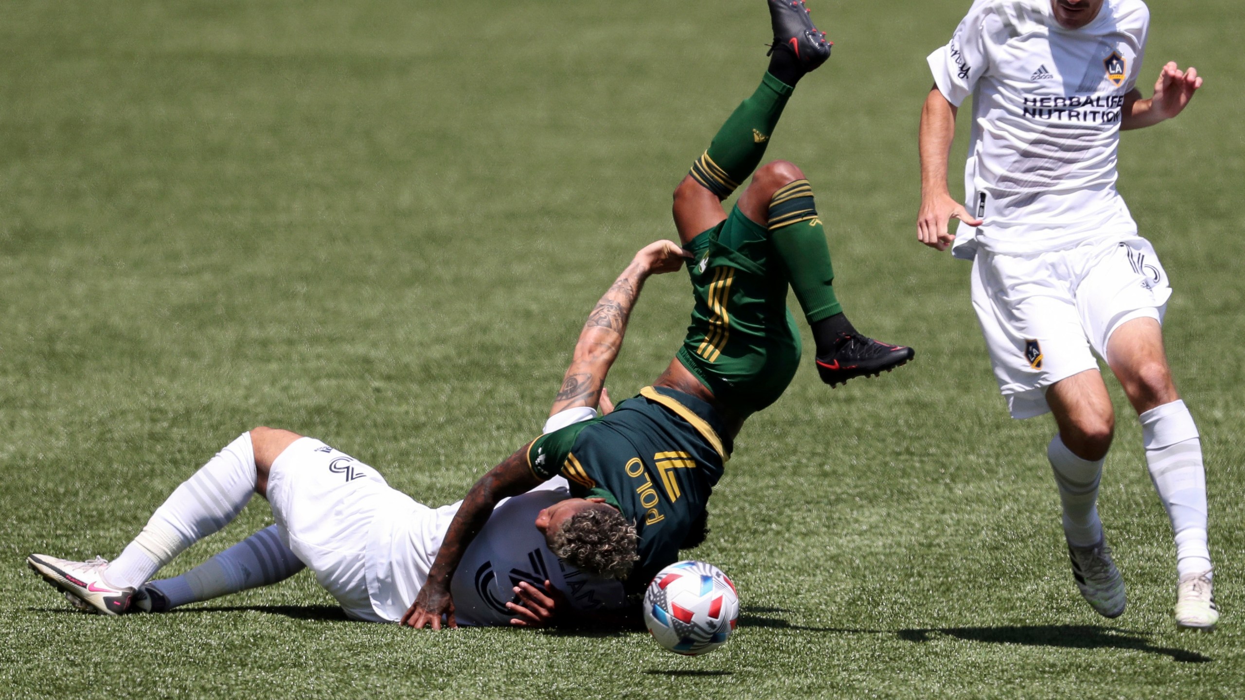 Portland Timbers midfielder Andy Polo (7) flips over Los Angeles Galaxy defender Derrick Williams (3) as L.A. Galaxy midfielder Sacha Kljestan (16) runs alongside them during the first half of an MLS soccer match on May 22, 2021, in Portland, Ore. Williams received a red card for the foul. (Amanda Loman / Associated Press)