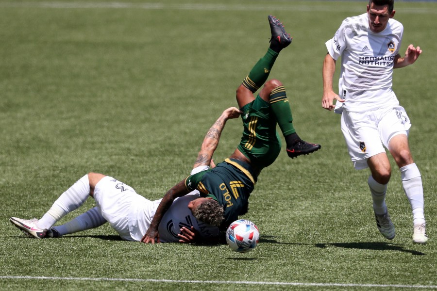 Portland Timbers midfielder Andy Polo (7) flips over Los Angeles Galaxy defender Derrick Williams (3) as L.A. Galaxy midfielder Sacha Kljestan (16) runs alongside them during the first half of an MLS soccer match on May 22, 2021, in Portland, Ore. Williams received a red card for the foul. (Amanda Loman / Associated Press)