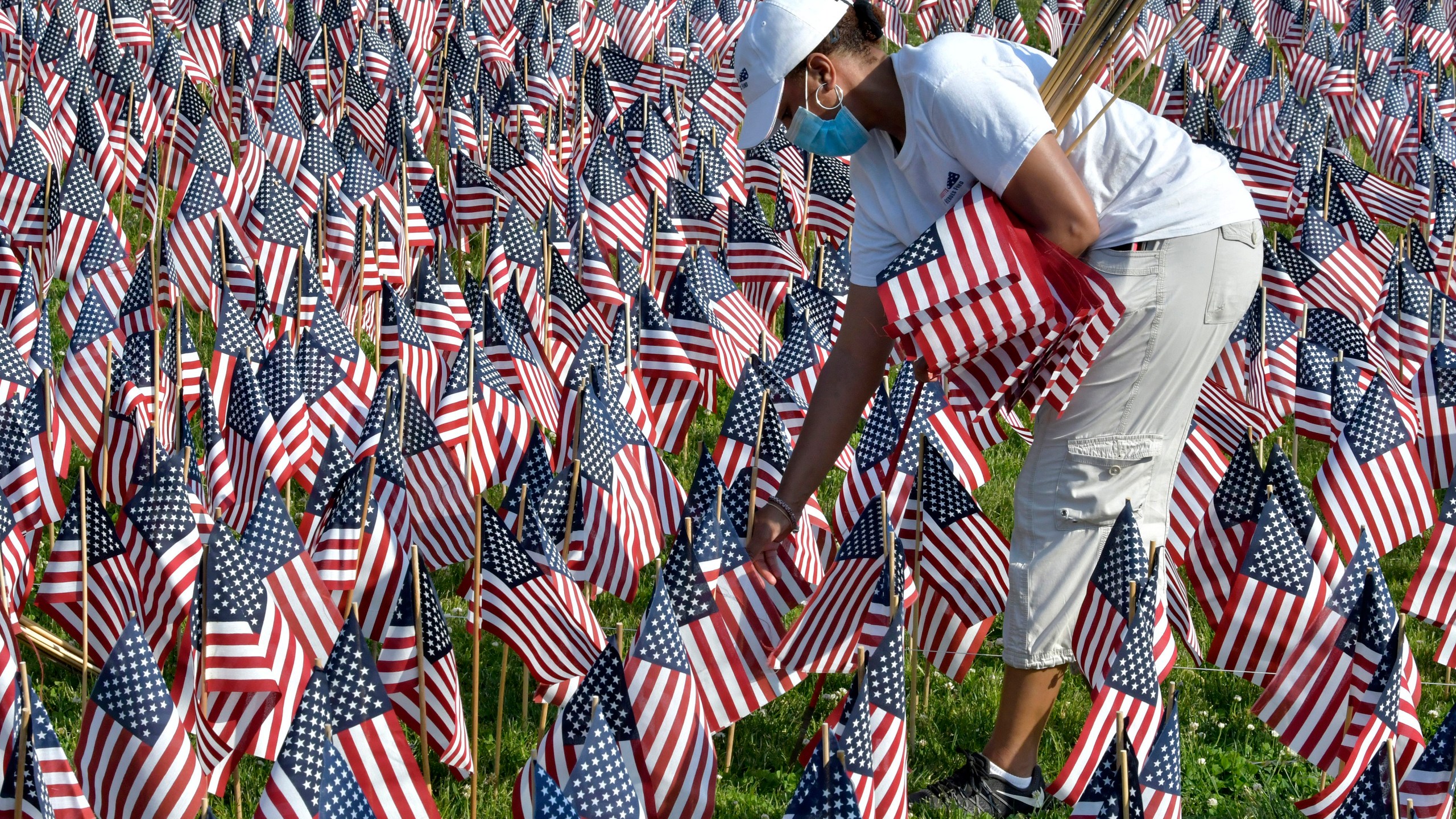 A volunteer places American flags on Boston Common ahead of Memorial Day, Wednesday. May 26, 2021, in Boston. After more than a year of isolation, American veterans are embracing plans for a more traditional Memorial Day. They say wreath-laying ceremonies, barbecues at local vets halls and other familiar events are a welcome chance to reconnect with fellow service members and renew solemn traditions honoring the nation’s war dead. (AP Photo/Josh Reynolds)