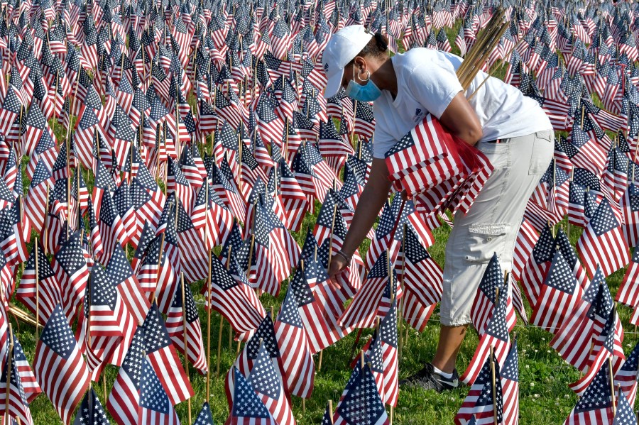 A volunteer places American flags on Boston Common ahead of Memorial Day, Wednesday. May 26, 2021, in Boston. After more than a year of isolation, American veterans are embracing plans for a more traditional Memorial Day. They say wreath-laying ceremonies, barbecues at local vets halls and other familiar events are a welcome chance to reconnect with fellow service members and renew solemn traditions honoring the nation’s war dead. (AP Photo/Josh Reynolds)