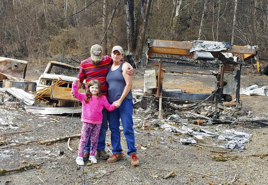 In this photo provided by Tye and Melynda Small, they are seen standing with their 5-year-old daughter, Madalyn, in front of the ruins of their home in Otis, Oregon after the Echo Mountain Fire in September, 2020. (Tye and Melynda Small via AP)