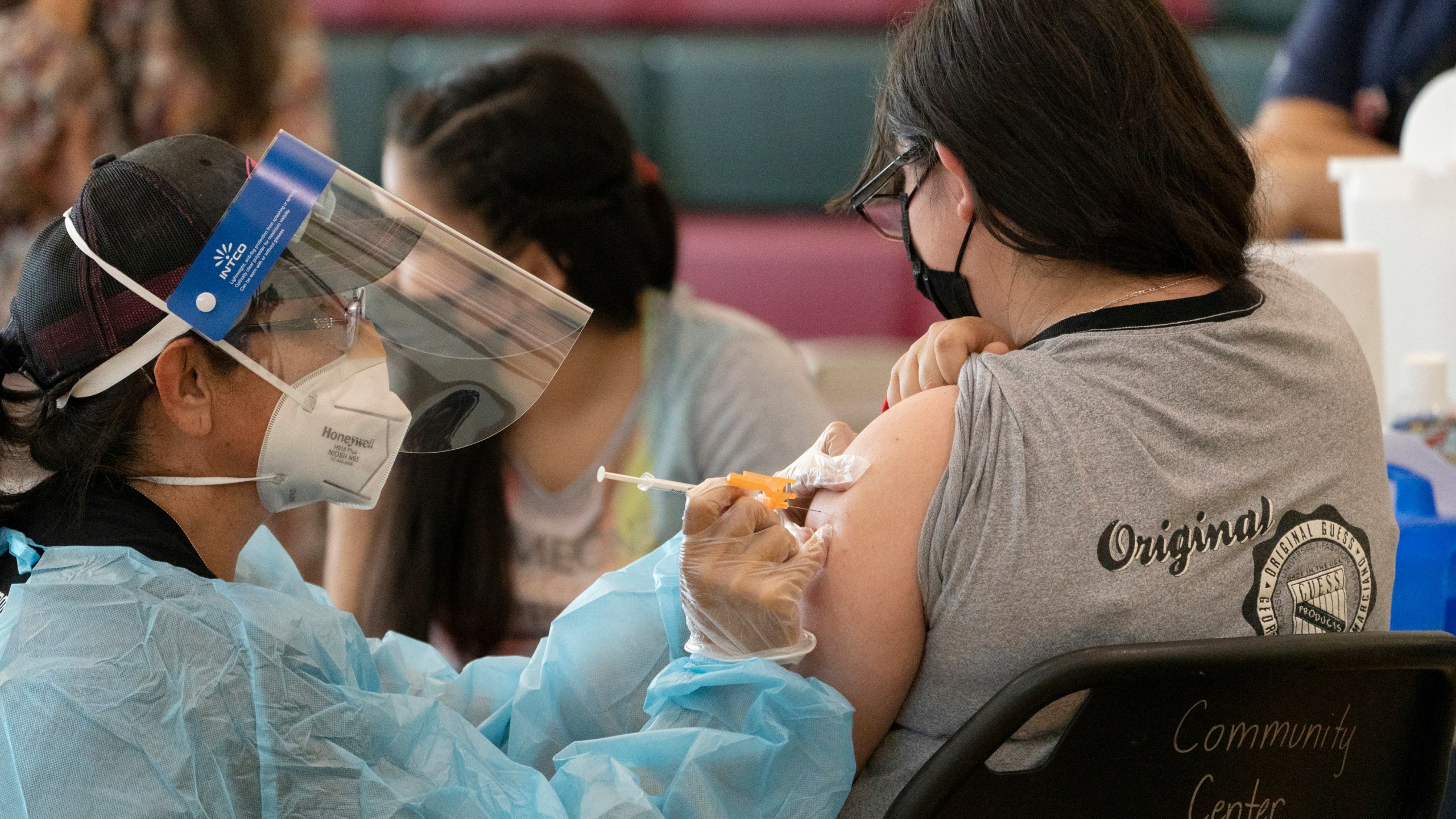 Sisters Guadalupe Flores, 15, right, and Estela Flores, 13, left, from East Los Angeles, get vaccinated with the Pfizer's COVID-19 vaccine by licensed vocational nurse Rita Orozco, far left, at the Esteban E. Torres High School in Los Angeles, Thursday, May 27, 2021. (AP Photo/Damian Dovarganes)