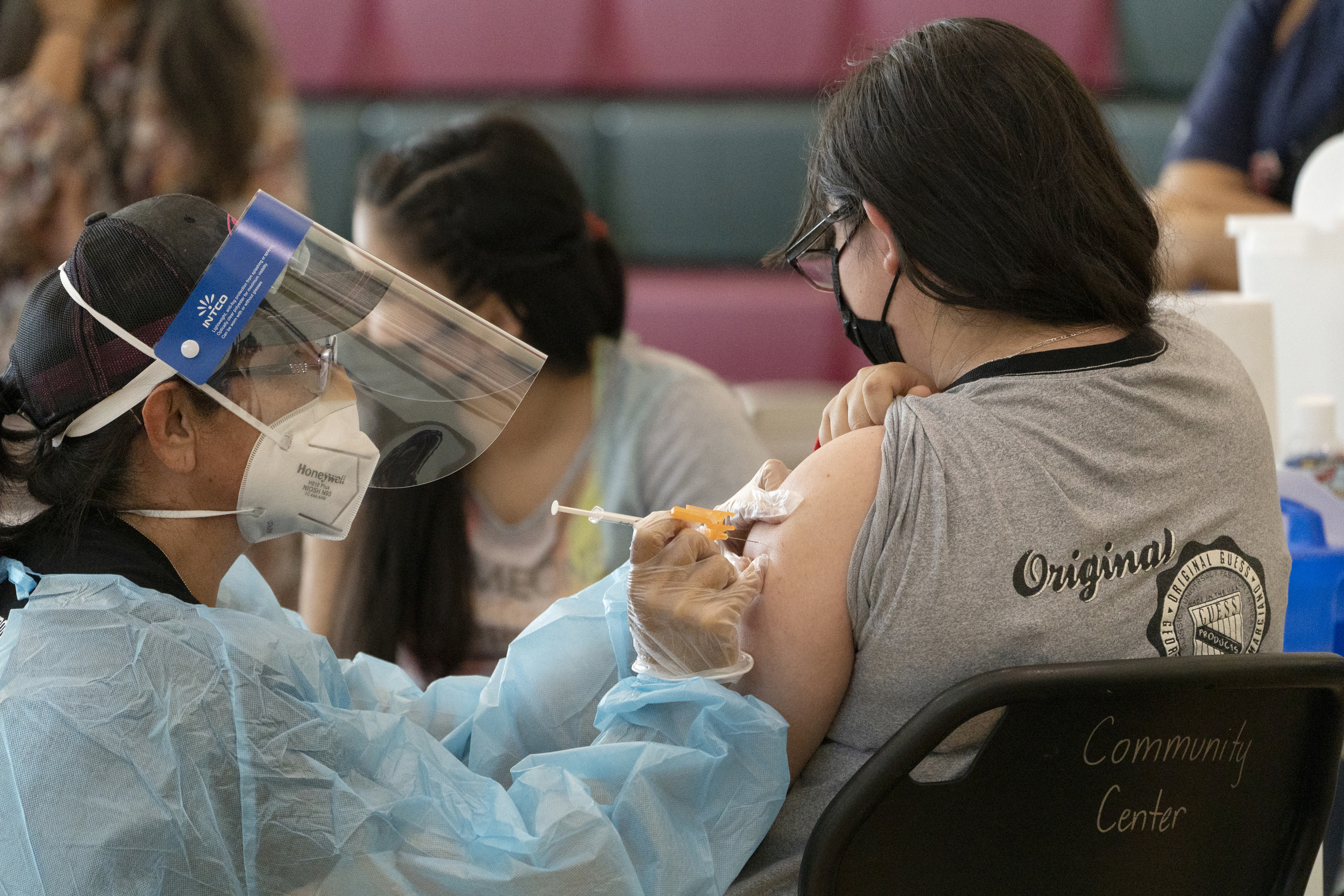 Sisters Guadalupe Flores, 15, right, and Estela Flores, 13, left, from East Los Angeles, get vaccinated with Pfizer's COVID-19 vaccine by licensed vocational nurse Rita Orozco, far left, at the Esteban E. Torres High School in Los Angeles on May 27, 2021. (Damian Dovarganes / Associated Press)