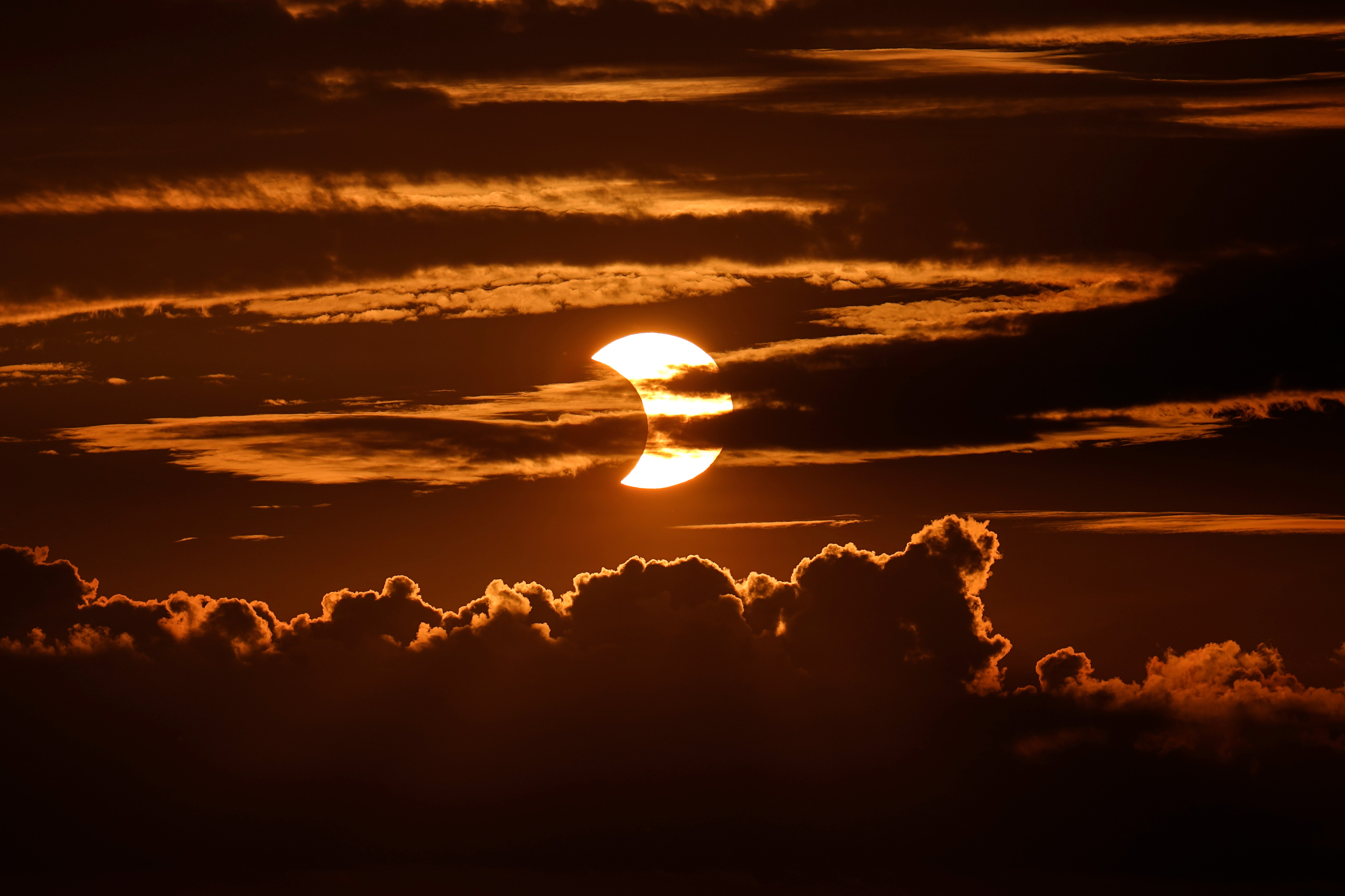 A partial solar eclipse rises behind clouds, Thursday, June 10, 2021, in Arbutus, Md. (AP Photo/Julio Cortez)