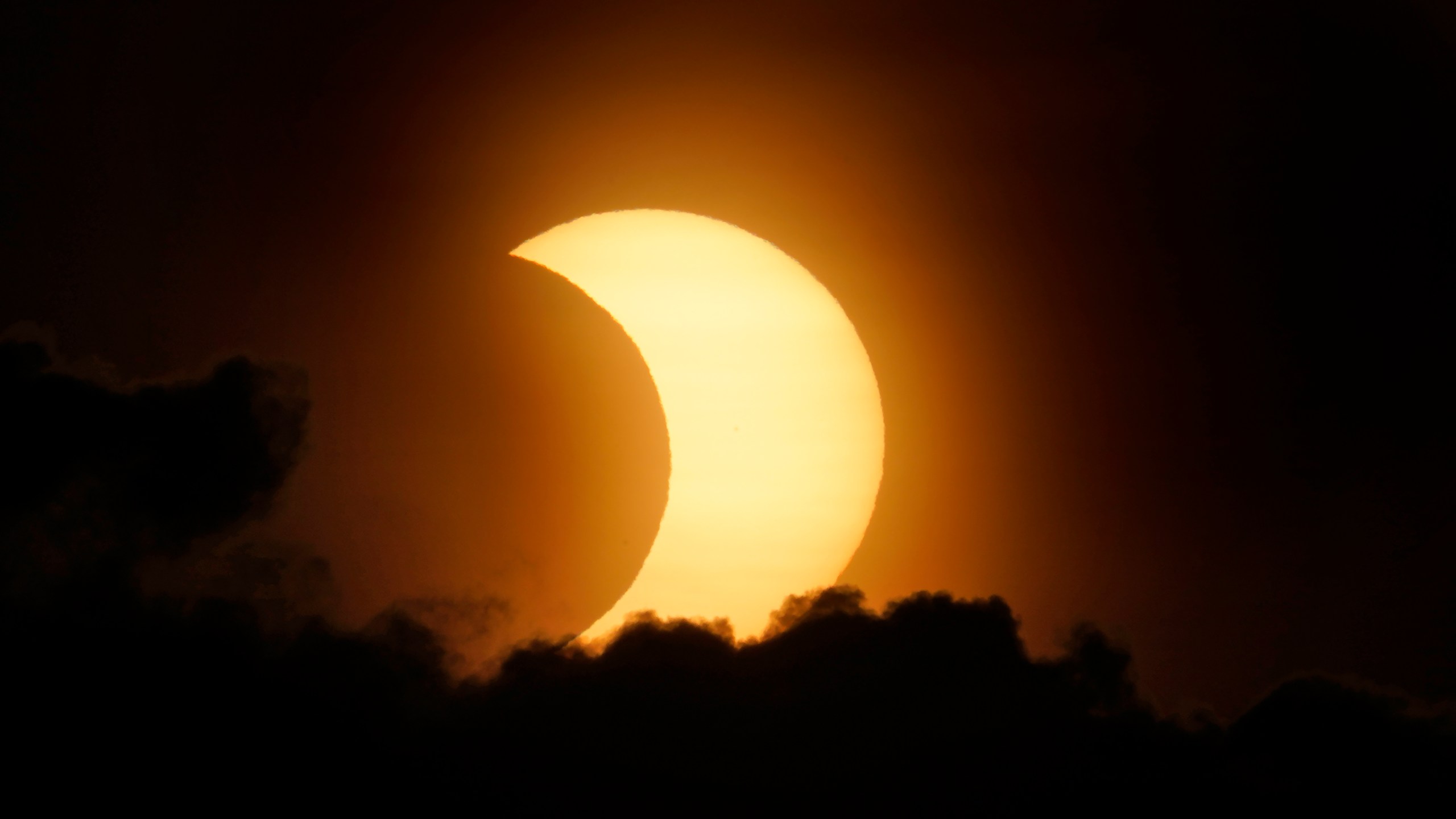 A partially eclipsed sun peaks out from behind a cloud as it rises over lower Manhattan in New York, Thursday, June 10, 2021. (AP Photo/Seth Wenig)