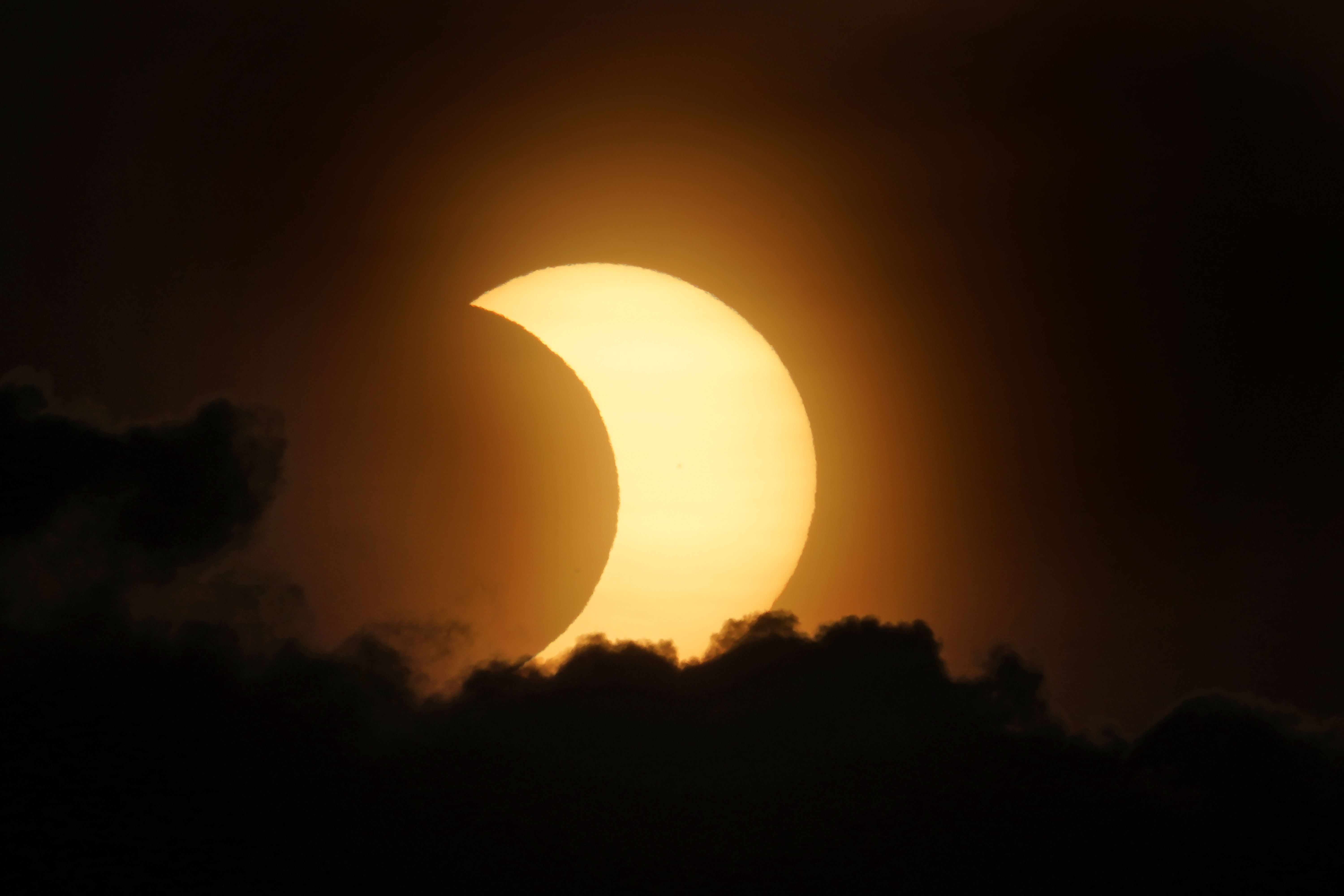 A partially eclipsed sun peaks out from behind a cloud as it rises over lower Manhattan in New York, Thursday, June 10, 2021. (AP Photo/Seth Wenig)