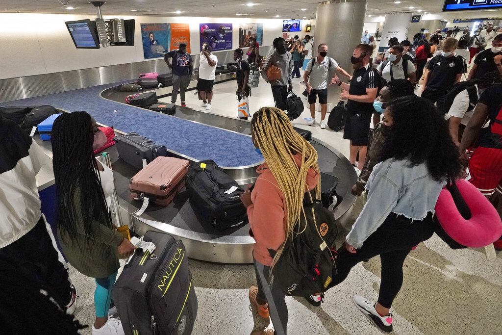 In this May 28, 2021 file photo, travelers wait for their luggage at a baggage carousel at Miami International Airport in Miami. (AP Photo/Wilfredo Lee, File)