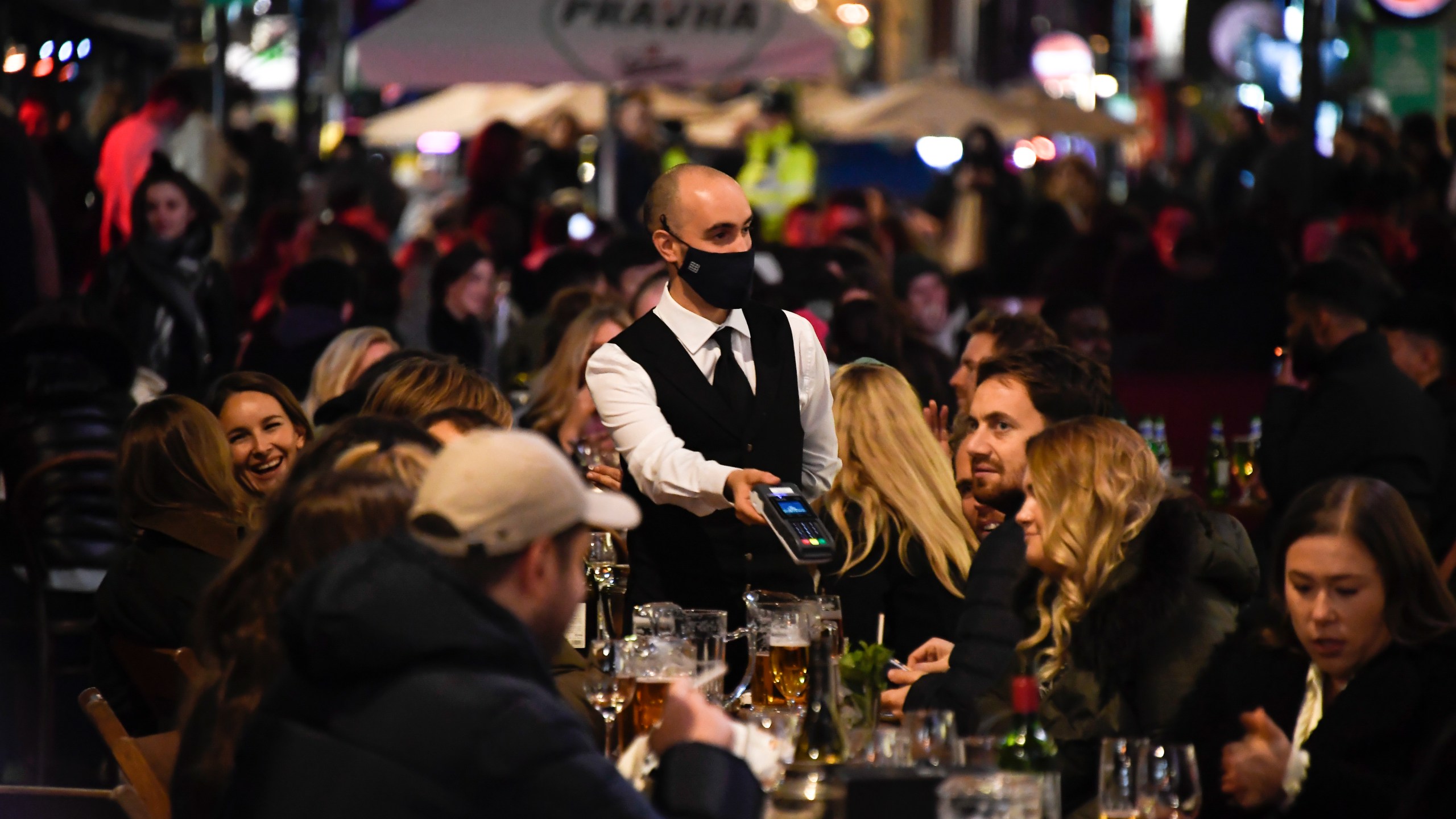 In this Wednesday, Nov. 4, 2020 file photo, a waiter wears a face mask as people eat and drink outside restaurants in Soho, in London. British Prime Minister Boris Johnson is expected to confirm Monday June 14, 2021, that the next planned relaxation of coronavirus restrictions in England will be delayed as a result of the spread of the delta variant first identified in India. (AP Photo/Alberto Pezzali, File)