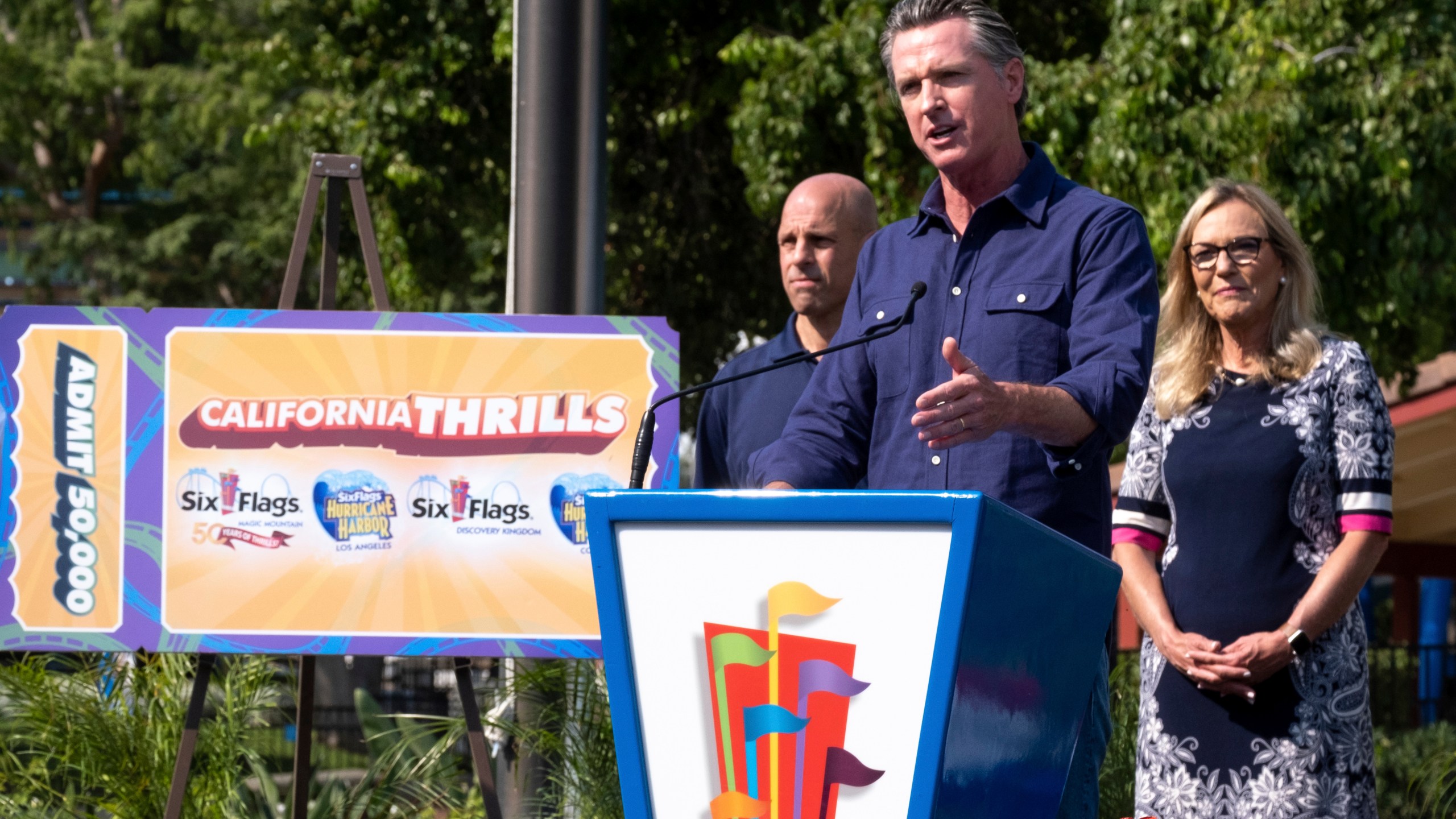 California Gov. Gavin Newsom welcomes the public to Six Flags Magic Mountain in Santa Clarita, Calif. Wednesday, June 16, 2021. At left, is Michael Spanos, President of Six Flags, at right is LA county supervisor Kathryn Barger. Newsom continued his tour of the state after lifting most COVID-19 restrictions Tuesday. (David Crane/The Orange County Register via AP)