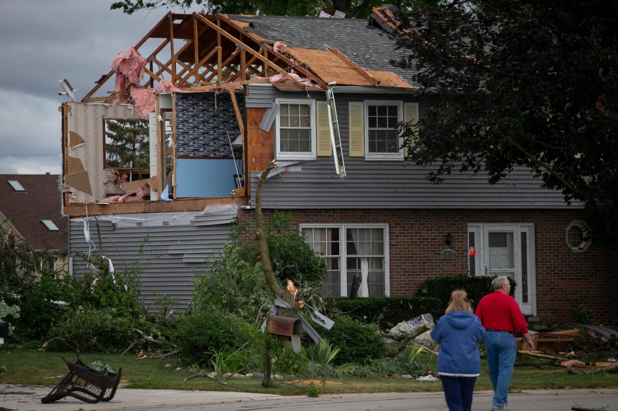 People walk near a damaged home on Princeton Circle in Naperville's Ranchview neighborhood after a tornado swept through the area, Monday, June 21, 2021, in Ill. (Rich Hein/Chicago Sun-Times via AP)