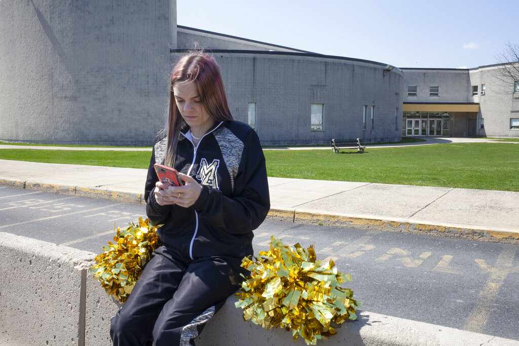 In this April 4, 2021, file photo provided by the American Civil Liberties Union, Brandi Levy wears her cheerleading outfit as she looks at her mobile phone outside Mahanoy Area High School in Mahanoy City, Pa. The Supreme Court ruled Wednesday, June 23, 2021, that the public school wrongly suspended Levy from cheerleading over a vulgar social media post she made after she didn't qualify for the varsity team. (Danna Singer/ACLU via AP, File)