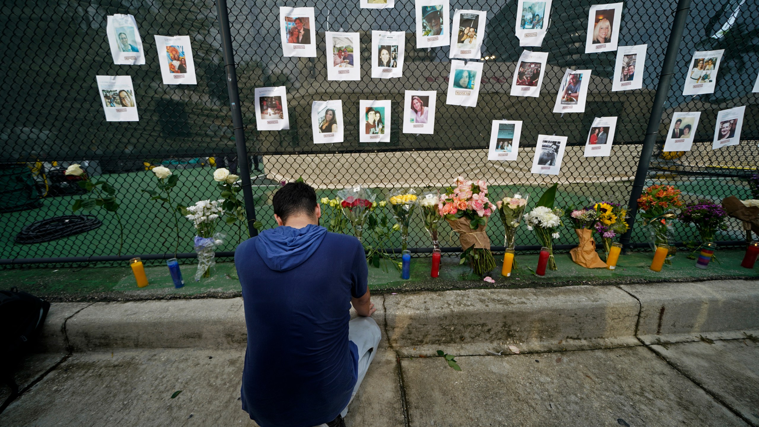 Leo Soto, who created this memorial with grocery stores donating flowers and candles, pauses in front of photos of some of the missing people that he put on a fence, near the site of an oceanfront condo building that partially collapsed in Surfside, Fla., Friday, June 25, 2021. (AP Photo/Gerald Herbert)