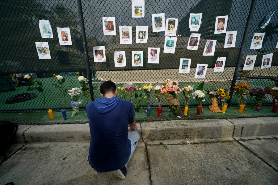 Leo Soto, who created this memorial with grocery stores donating flowers and candles, pauses in front of photos of some of the missing people that he put on a fence, near the site of an oceanfront condo building that partially collapsed in Surfside, Fla., Friday, June 25, 2021. (AP Photo/Gerald Herbert)