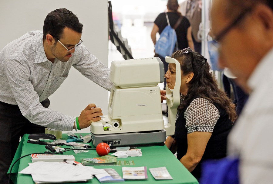 In this Oct. 1, 2013, file photo, Rosa Guerra, 52, right, gets a free eye exam during the Binational Health Week event held at the Mexican Consulate in Los Angeles. (AP Photo/Damian Dovarganes, File)