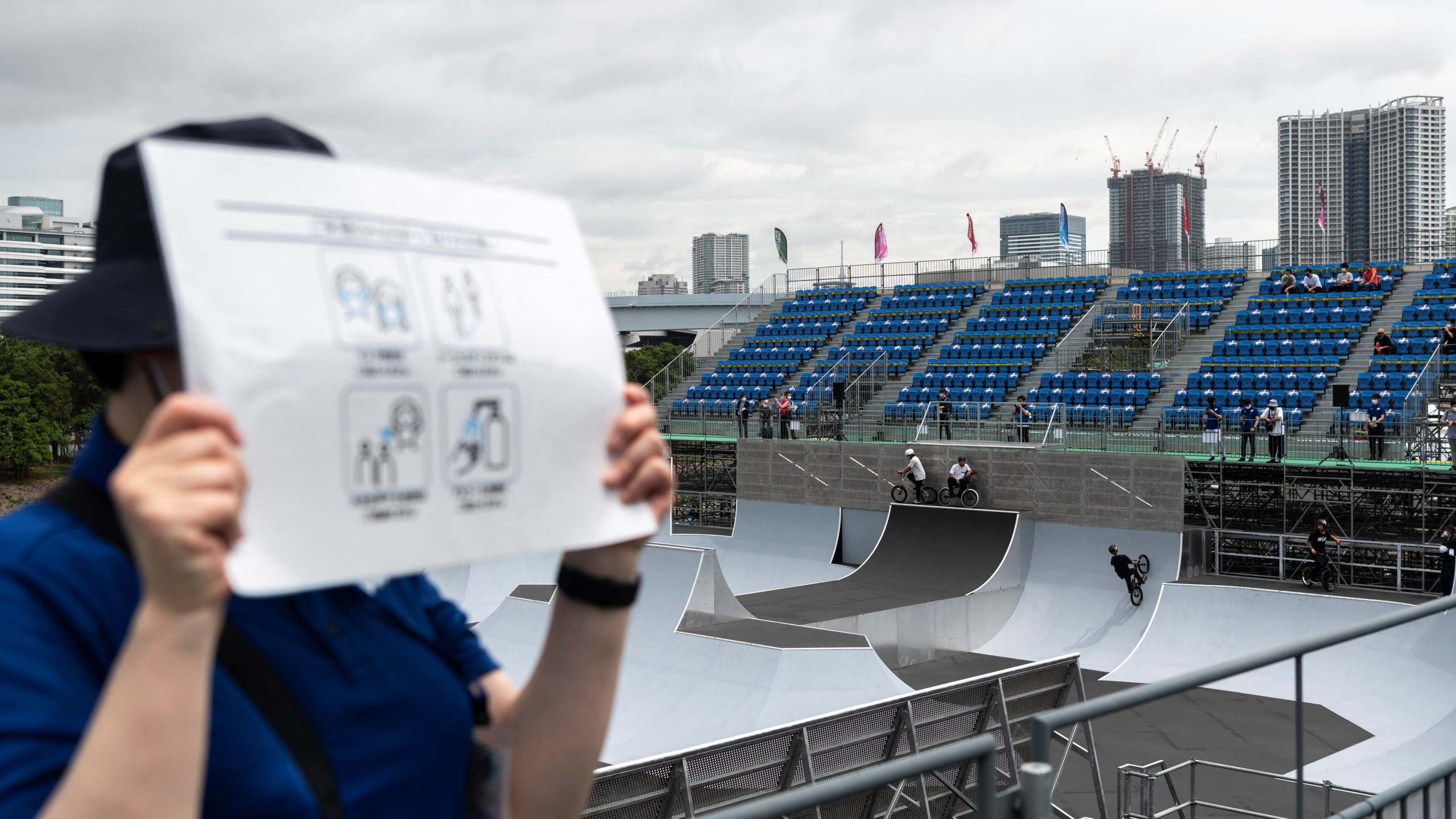 A volunteer holds a poster with measures against covid19 propagation in the BMX freestyle track venue during a test event for the Tokyo 2020 Olympic Games at Ariake Urban Sports Park in Tokyo on May 17, 2021. (CHARLY TRIBALLEAU / AFP)