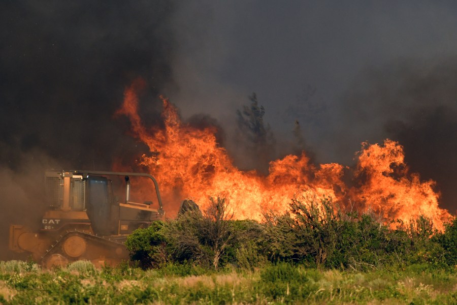 A bulldozer operator works on a fire line as vegetation burns nearby at the Lava Fire on Monday, June 28, 2021, north of Weed, Calif. Officers shot and killed a man who pulled a gun as they tried to keep him out of a complex of marijuana farms in an area of far Northern California where thousands of people have been ordered to evacuate because of a raging wildfire. (Scott Stoddard/Grants Pass Daily Courier via AP)