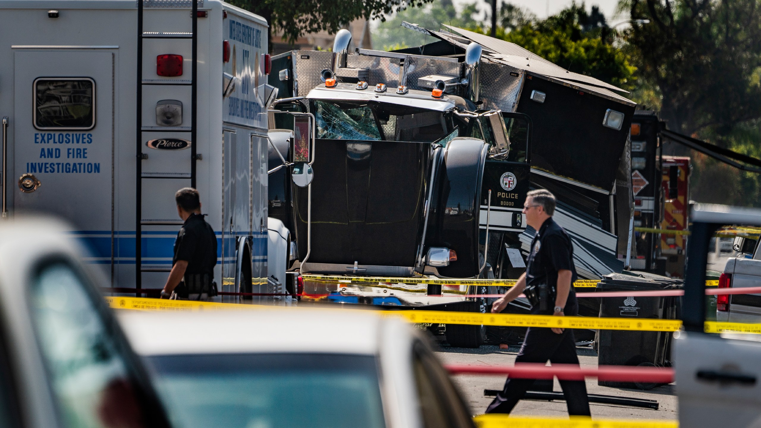 Police officers walk past the remains of an armored Los Angeles Police Department tractor-trailer on July 1, 2021, the morning after illegal fireworks seized at a South Los Angeles home exploded. (Damian Dovarganes / Associated Press)