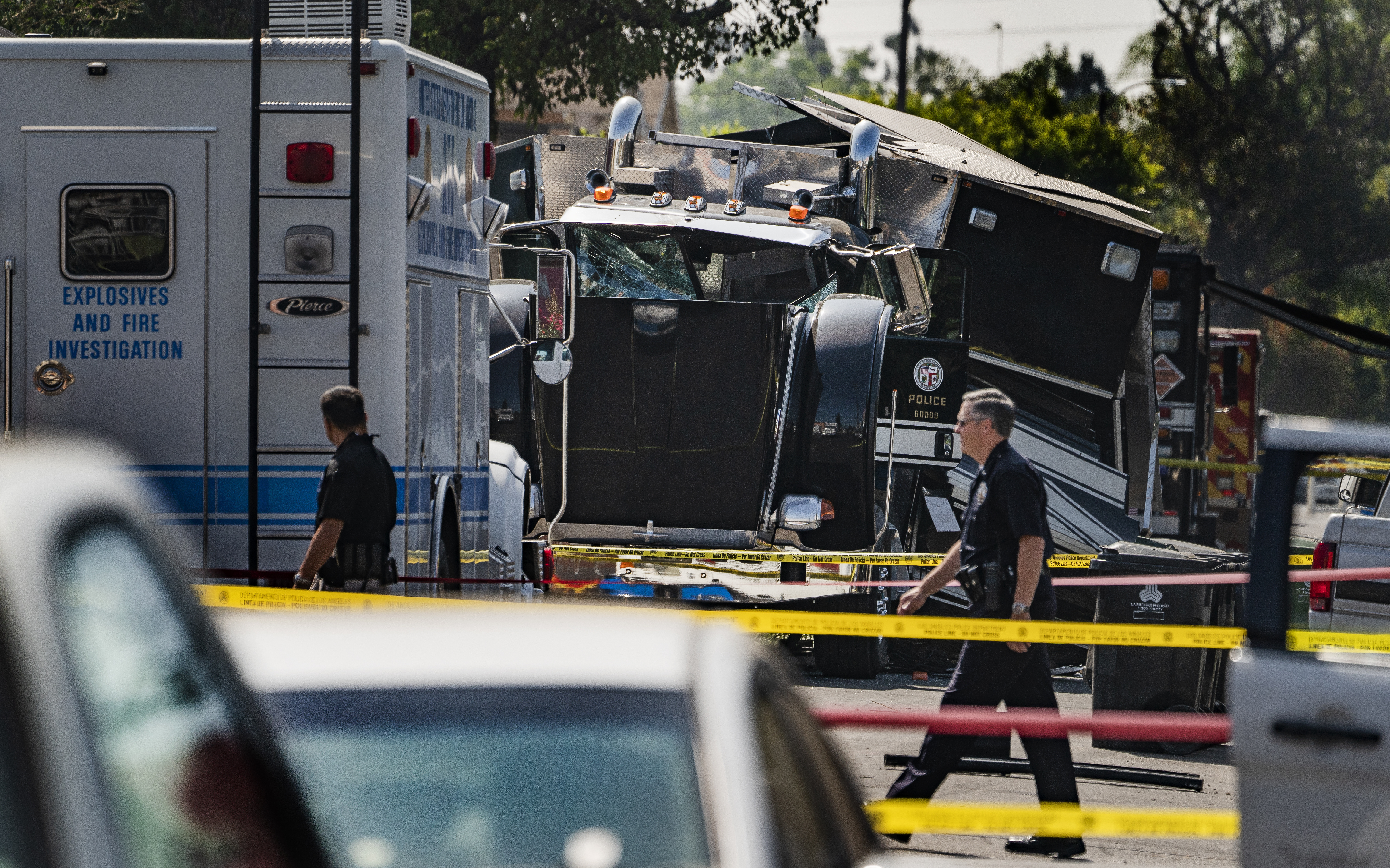 Police officers walk past the remains of an armored Los Angeles Police Department tractor-trailer on July 1, 2021, the morning after illegal fireworks seized at a South Los Angeles home exploded. (Damian Dovarganes / Associated Press)