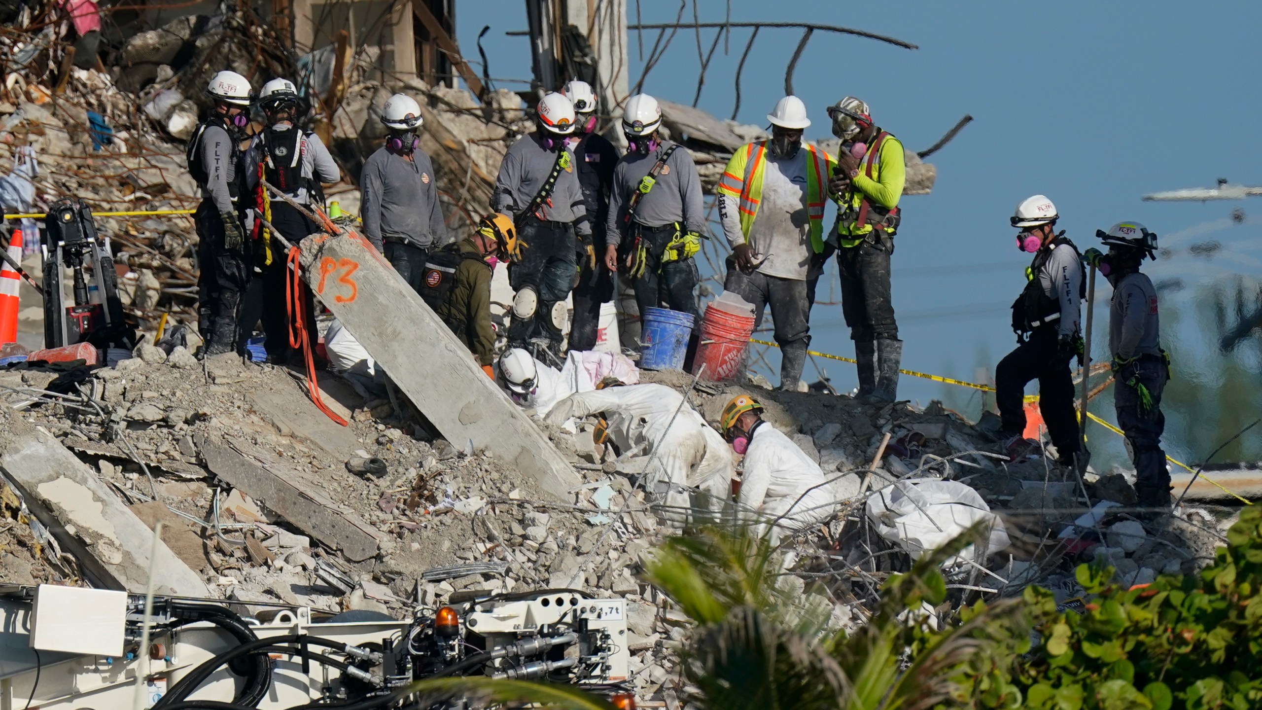 A team works to extricate remains as search and rescue personnel look on, atop the rubble at the Champlain Towers South condo building where scores of people remain missing more than a week after it partially collapsed, Friday, July 2, 2021, in Surfside, Fla. Rescue efforts resumed Thursday evening after being halted for most of the day over concerns about the stability of the remaining structure.(AP Photo/Mark Humphrey)