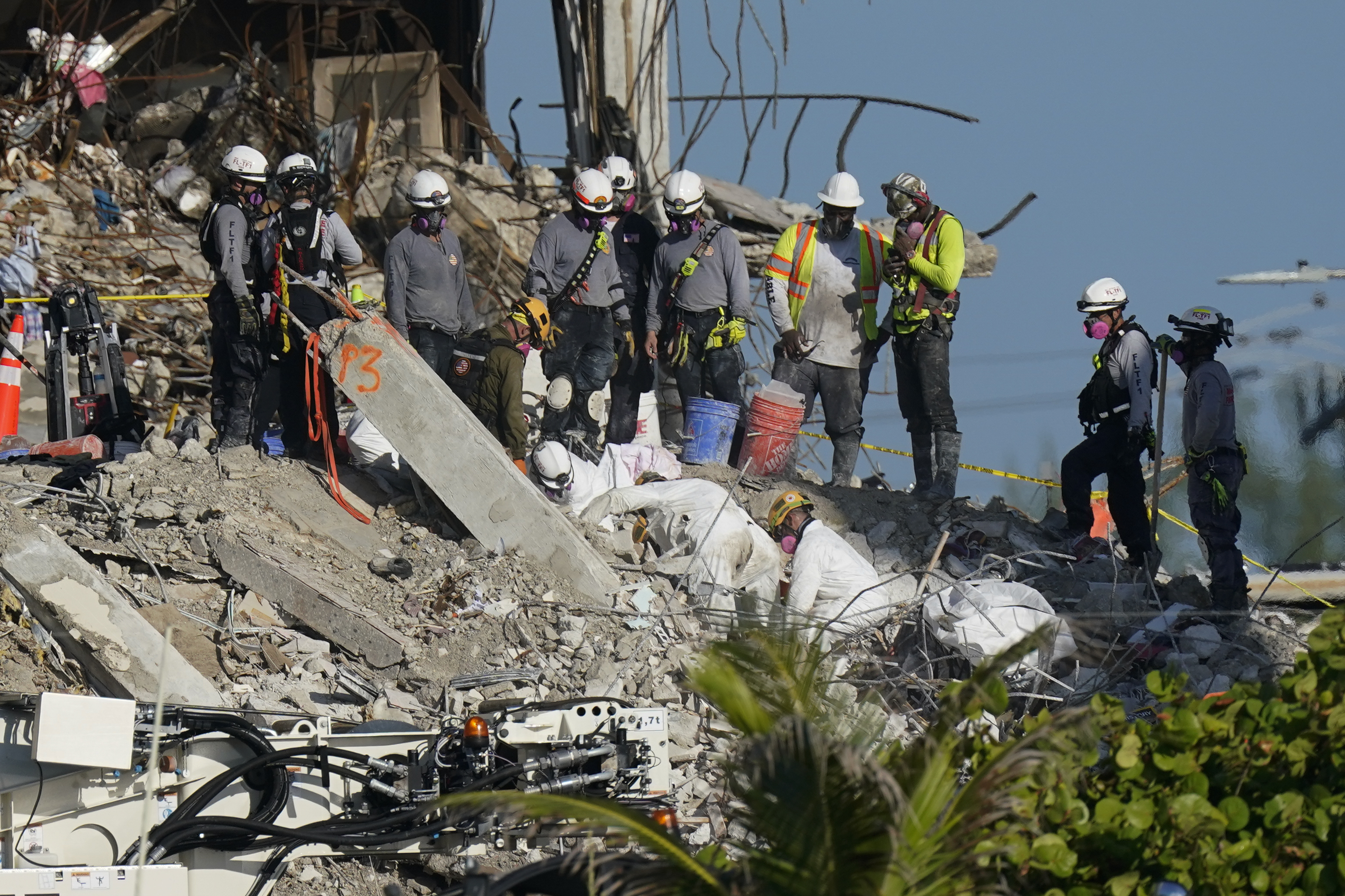 A team works to extricate remains as search and rescue personnel look on, atop the rubble at the Champlain Towers South condo building where scores of people remain missing more than a week after it partially collapsed, Friday, July 2, 2021, in Surfside, Fla. Rescue efforts resumed Thursday evening after being halted for most of the day over concerns about the stability of the remaining structure.(AP Photo/Mark Humphrey)