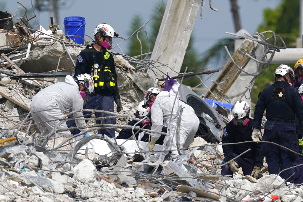 Rescue workers handle a tarp containing recovered remains at the site of the collapsed Champlain Towers South condo building, Monday, July 5, 2021, in Surfside, Fla. (AP Photo/Lynne Sladky)