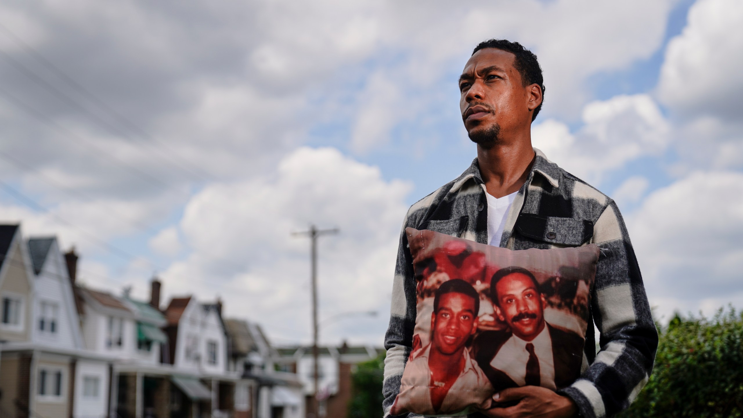 In this July 9, 2021, photo Brett Roman Williams poses for a photograph while holding a pillow with a photo of his father, Donald Williams, lower right, and brother Derrick Williams who both were killed by gunfire 20 years apart, in Philadelphia. (AP Photo/Matt Rourke)