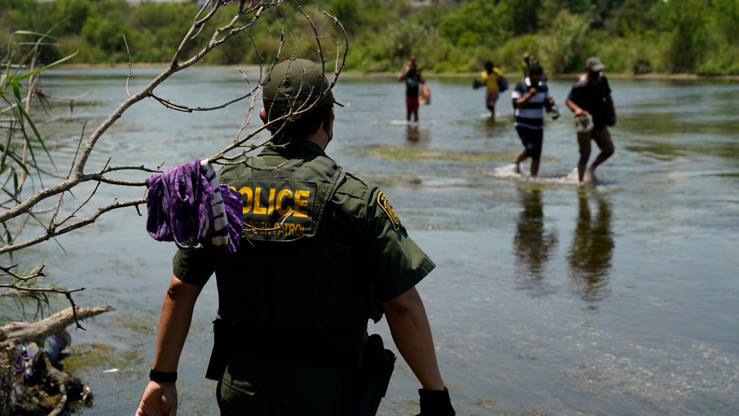 In this June 15, 2021, file photo, a Border Patrol agent watches as a group of migrants walk across the Rio Grande on their way to turning themselves in upon crossing the U.S.-Mexico border in Del Rio, Texas. A Justice Department attorney says the U.S. Centers for Disease Control and Prevention will issue an order this week about treatment of children under a public health order that has prevented migrants from seeking asylum at U.S. borders. (AP Photo/Eric Gay, File)