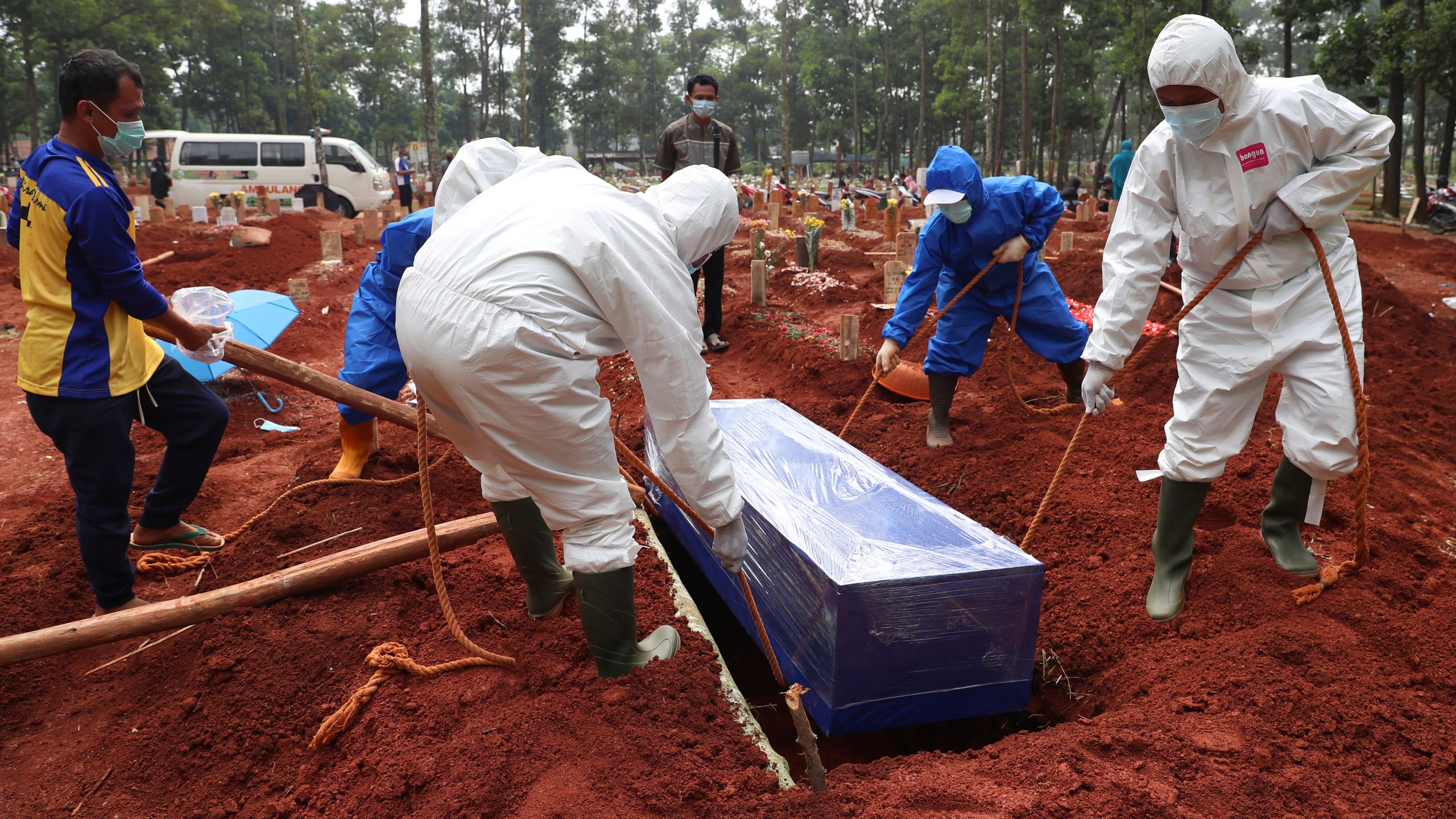 Workers in protective gear lower a coffin of a COVID-19 victim to a grave for burial at the Cipenjo Cemetery in Bogor, West Java, Indonesia on July 14, 2021. (Achmad Ibrahim/Associated Press)