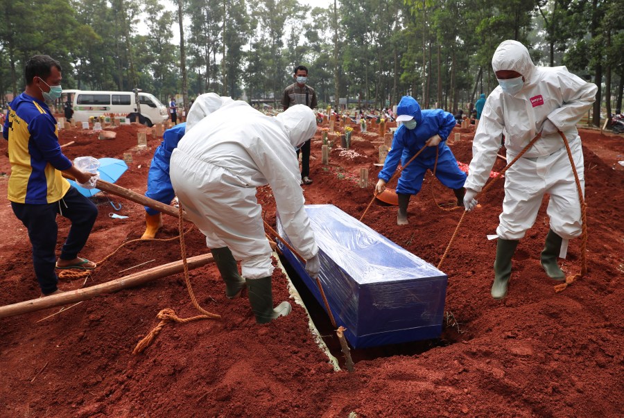 Workers in protective gear lower a coffin of a COVID-19 victim to a grave for burial at the Cipenjo Cemetery in Bogor, West Java, Indonesia on July 14, 2021. (Achmad Ibrahim/Associated Press)