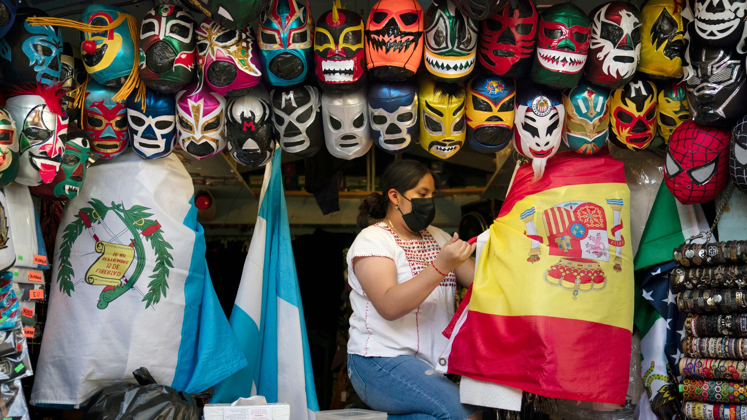 In this June 8, 2021, file photo, clerk Wendy Ramirez uses a Spanish flag to wrap souvenirs while preparing to close the store for the day on Olvera Street in Los Angeles. Los Angeles County residents are again required to wear masks indoors regardless of their vaccination status, a new mandate starting this weekend that health officials hope will reverse the latest spikes in coronavirus cases, hospitalizations and deaths. The rule went into effect late Saturday, July 17, for the nation's largest county, home to 11 million people, where a sharp increase in COVID-19 cases is led by the highly transmissible delta variant. (AP Photo/Jae C. Hong, File)