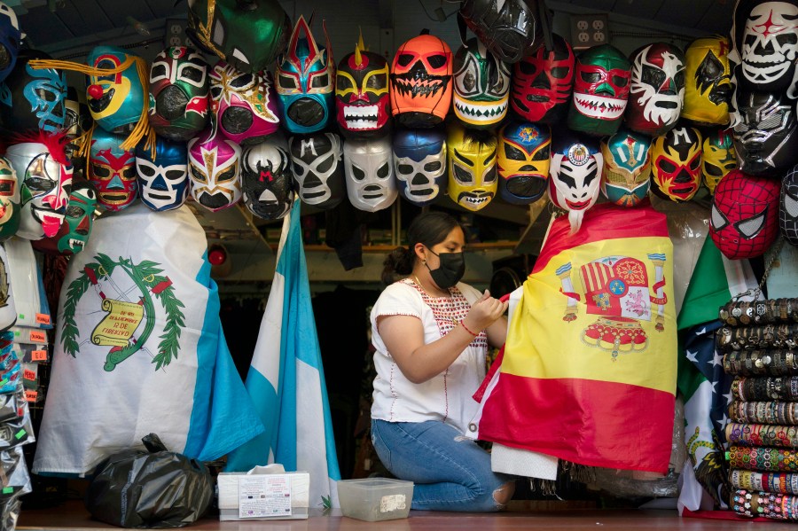 In this June 8, 2021, file photo, clerk Wendy Ramirez uses a Spanish flag to wrap souvenirs while preparing to close the store for the day on Olvera Street in Los Angeles. Los Angeles County residents are again required to wear masks indoors regardless of their vaccination status, a new mandate starting this weekend that health officials hope will reverse the latest spikes in coronavirus cases, hospitalizations and deaths. The rule went into effect late Saturday, July 17, for the nation's largest county, home to 11 million people, where a sharp increase in COVID-19 cases is led by the highly transmissible delta variant. (AP Photo/Jae C. Hong, File)