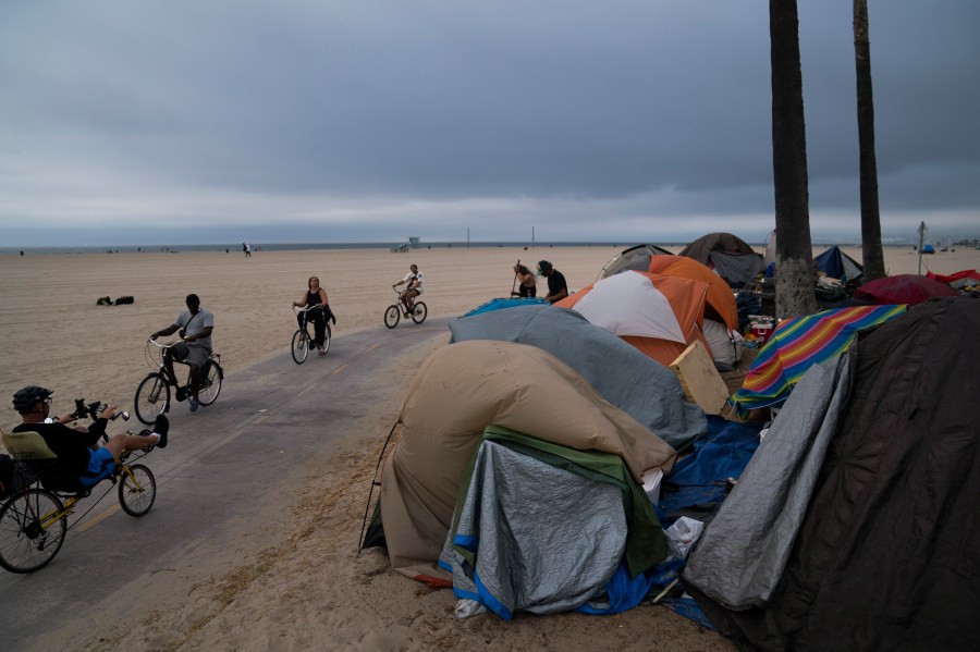 People ride their bikes past a homeless encampment set up along the boardwalk in the Venice neighborhood of Los Angeles, Tuesday, June 29, 2021. The proliferation of homeless encampments on Venice Beach has sparked an outcry from residents and created a political spat among Los Angeles leaders. (AP Photo/Jae C. Hong)