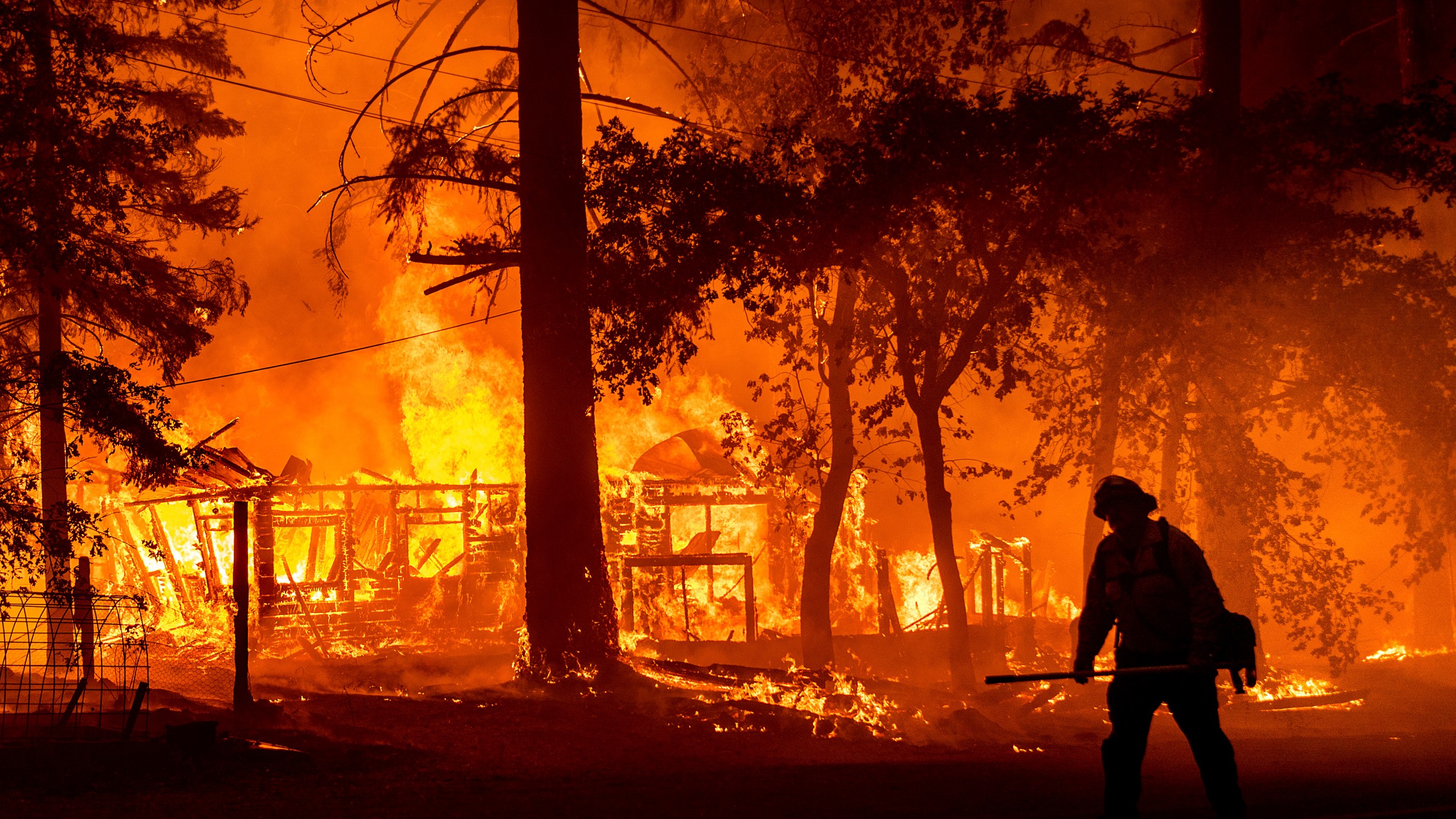 In this Saturday, July 24, 2021, file photo a firefighter passes a burning home as the Dixie Fire flares in Plumas County, Calif. The fire destroyed multiple residences as it tore through the Indian Falls community. Erratic winds and the potential for dry lightning added to the challenges facing firefighters battling California's largest wildfire, one of numerous blazes burning Monday across the U.S. West. (AP Photo/Noah Berge,File)