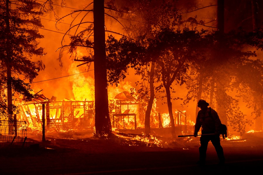 In this Saturday, July 24, 2021, file photo a firefighter passes a burning home as the Dixie Fire flares in Plumas County, Calif. The fire destroyed multiple residences as it tore through the Indian Falls community. Erratic winds and the potential for dry lightning added to the challenges facing firefighters battling California's largest wildfire, one of numerous blazes burning Monday across the U.S. West. (AP Photo/Noah Berge,File)