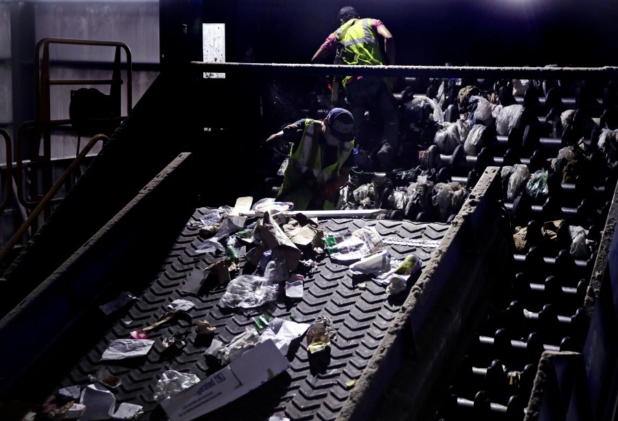 In this Thursday, Sept. 6, 2018, file photo, workers clean consumer plastic shopping bags from the clogged rollers of a machine which separates paper, plastic and metal recyclable material, in a processing building at EL Harvey & Sons, a waste and recycling company, in Westborough, Mass. (AP Photo/Charles Krupa, File)