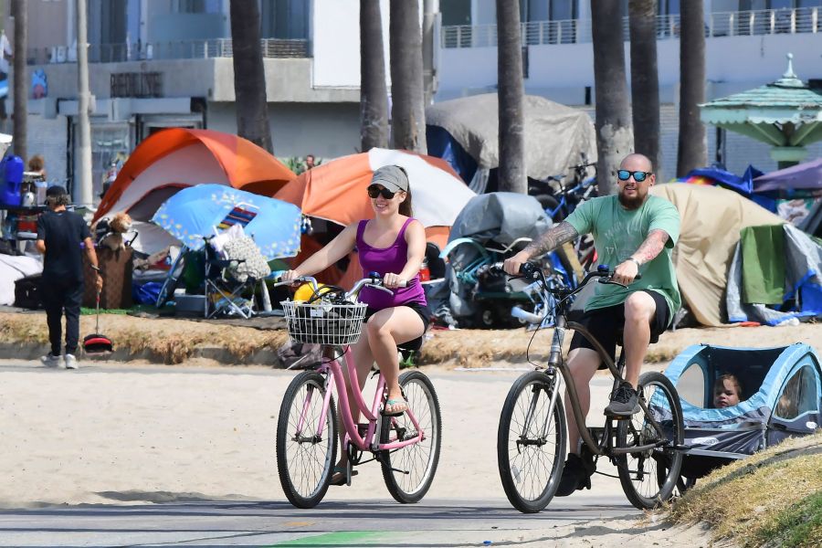 Cyclists ride past tents housing the homeless along the Ocean Front Walk in Venice, California on June 30, 2021, where an initiative began this week offering people in homeless encampments a voluntary path to permanent housing. (Frederic J. Brown AFP via Getty Images)