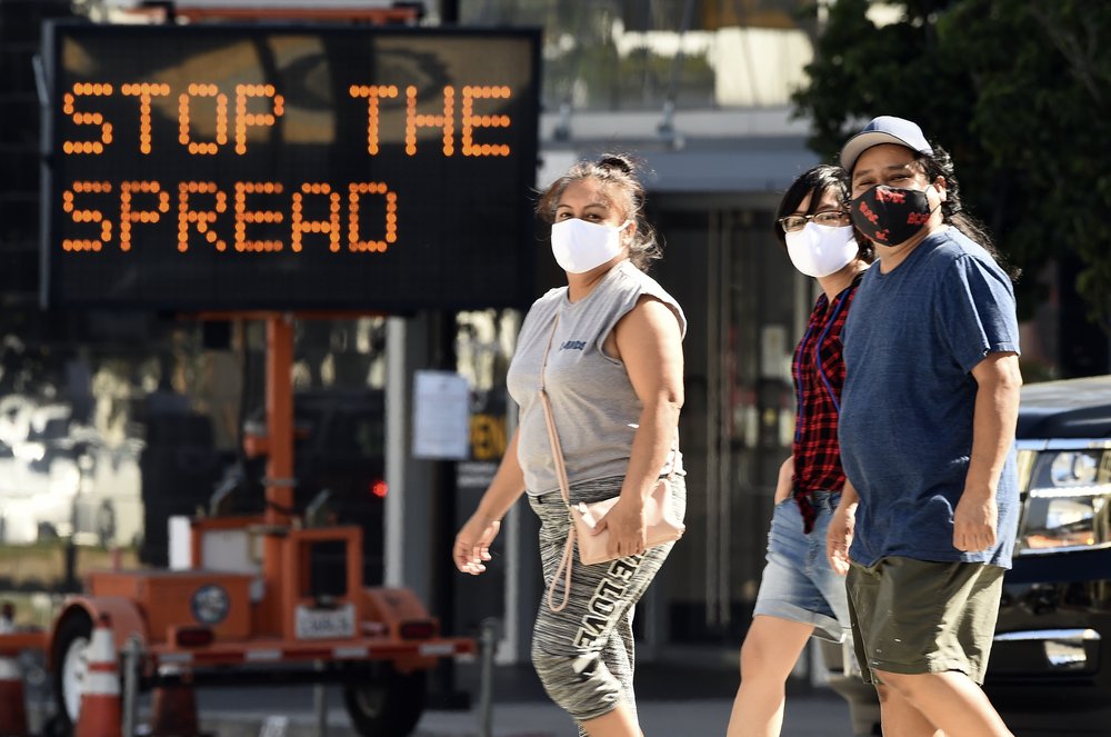 Pedestrians wear masks as they walk in front of a sign reminding the public to take steps to stop the spread of coronavirus on July 23, 2020, in Glendale, Calif. (AP Photo/Chris Pizzello, File)