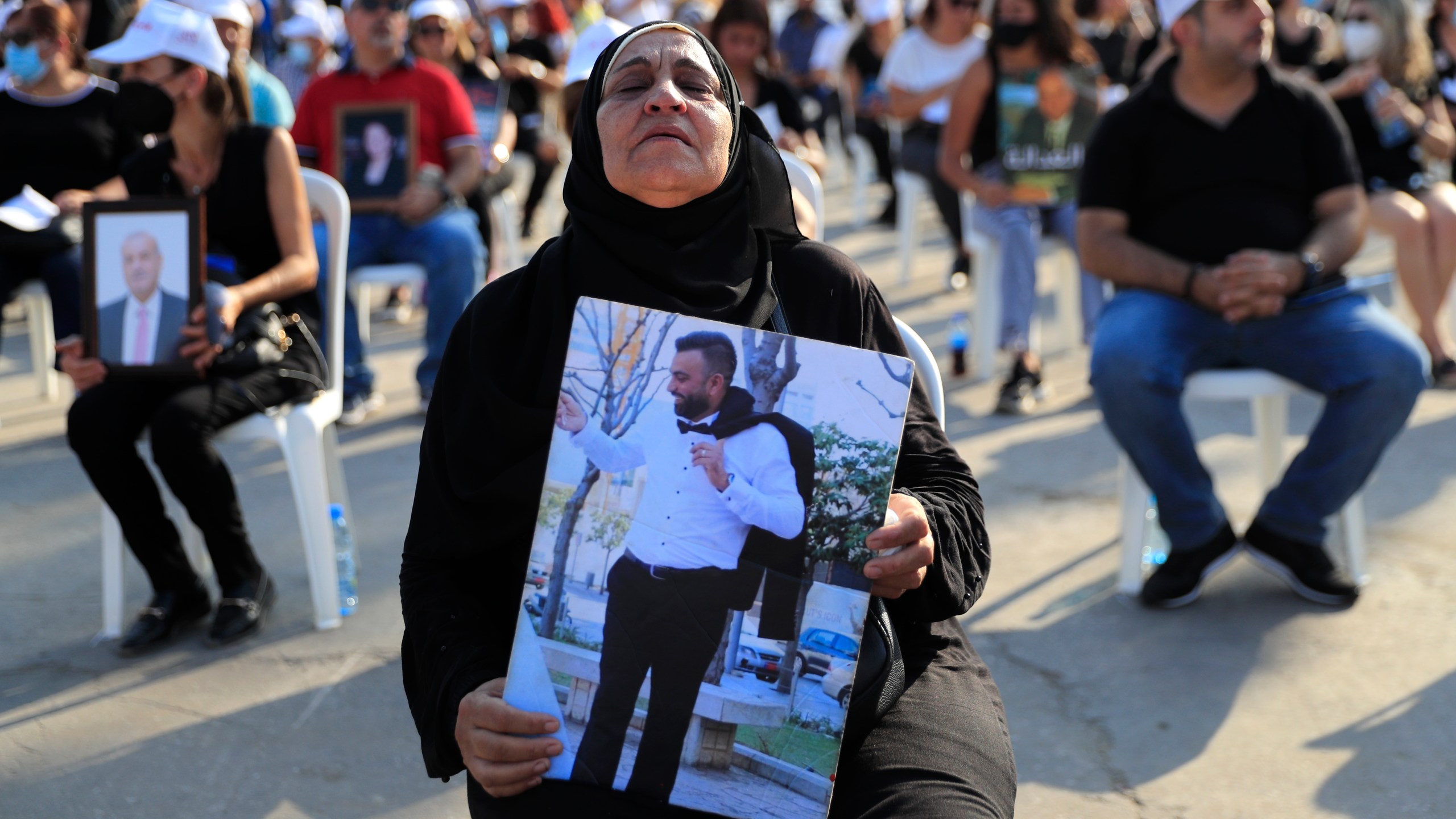 The mother of a victim who was killed in the massive blast last year at the Beirut port holds a portrait of her son as she attends a Mass held to commemorate the first year anniversary of the deadly blast, at the Beirut port in Lebanon on Aug. 4, 2021. United in grief and anger, families of the victims and other Lebanese came out into the streets of Beirut on Wednesday to demand accountability as banks, businesses and government offices shuttered to mark one year since the horrific explosion. (AP Photo/Hussein Malla)