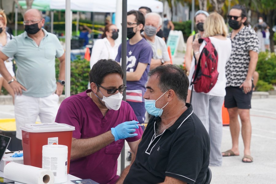 Carlos Anacleto closes his eyes as he receives the Pfizer COVID-19 vaccine from nurse Jorge Tase, as others wait their turn, Wednesday, Aug. 4, 2021, in Miami Beach, Fla. (AP Photo/Marta Lavandier)