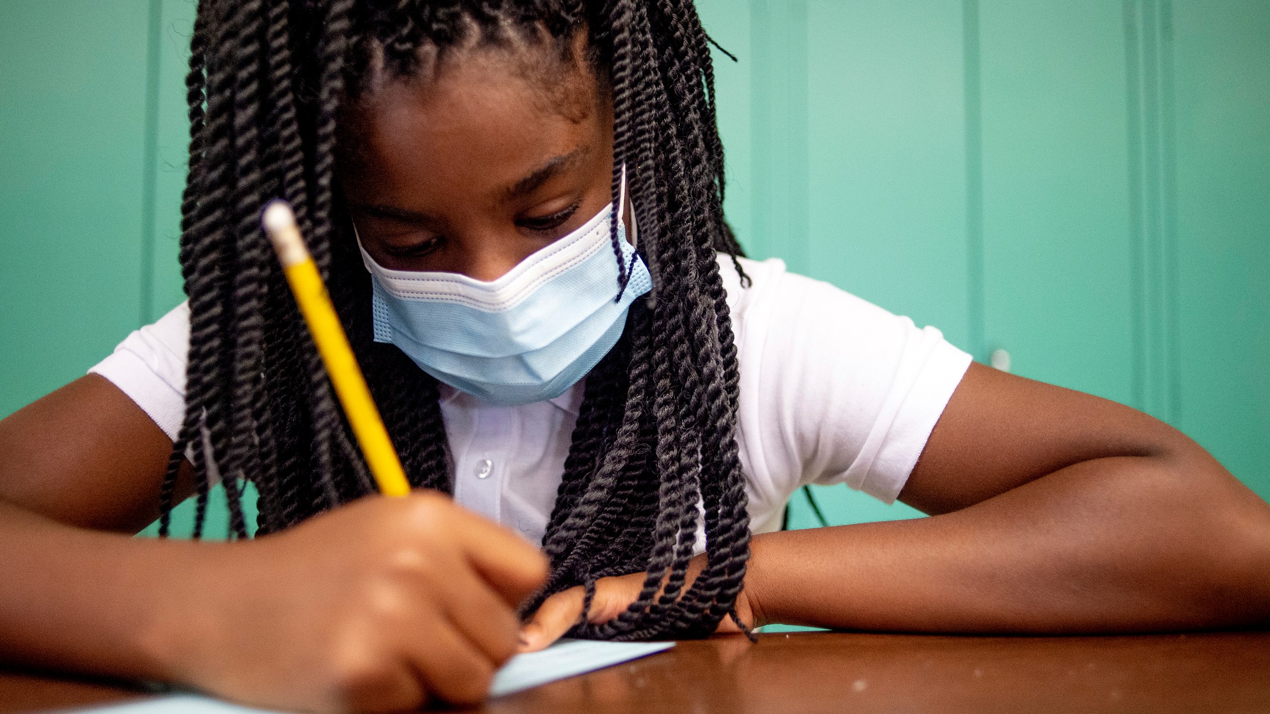 Sixth-grader Adriana Campbell, 11, jots down her name as she starts to work on her first assignment during the first day of school on Wednesday, Aug. 4, 2021 at Freeman Elementary School in Flint, Mich. (Jake May/The Flint Journal via AP)