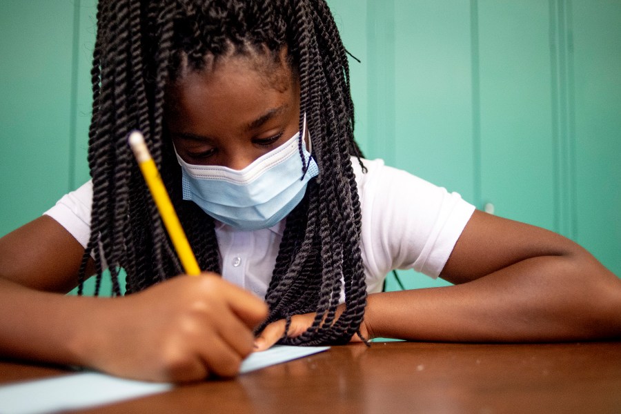 Sixth-grader Adriana Campbell, 11, jots down her name as she starts to work on her first assignment during the first day of school on Wednesday, Aug. 4, 2021 at Freeman Elementary School in Flint, Mich. (Jake May/The Flint Journal via AP)