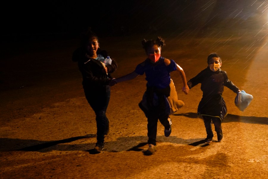 In this May 11, 2021 file photo three young migrants hold hands as they run in the rain at an intake area after turning themselves in upon crossing the U.S.-Mexico border in Roma, Texas. An official says the Biden administration has begun flying some Central American families deep into Mexico as authorities encounter more families and unaccompanied children at the U.S.-Mexico border. (AP Photo/Gregory Bull, File)