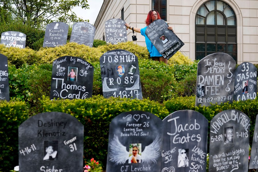 Jayde Newton helps to set up cardboard gravestones with the names of victims of opioid abuse outside the courthouse where the Purdue Pharma bankruptcy is taking place in White Plains, N.Y., Monday, Aug. 9, 2021. Purdue Pharma's quest to settle thousands of lawsuits over the toll of OxyContin is entering its final phase with the grudging acceptance of most of those with claims against the company. (AP Photo/Seth Wenig)