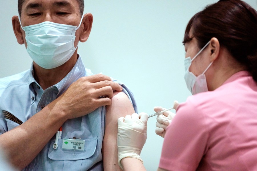 In this July 1, 2021, file photo, a Tokyo Metropolitan government employee takes the Moderna's COVID-19 vaccine shot at a vaccination center in the government building in Tokyo. The Tokyo Olympics are over, but it's still vacation season in Japan, and many are ignoring government pleas to avoid travel and stay away from bars and restaurants even as the coronavirus spikes at record levels. (AP Photo/Eugene Hoshiko, File)