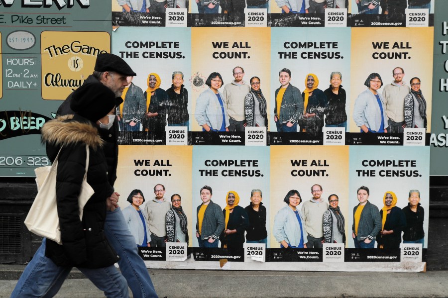 In this Wednesday, April 1, 2020 file photo, People walk past posters encouraging participation in the 2020 Census in Seattle's Capitol Hill neighborhood. From McKenzie County, North Dakota to St. Johns County Florida, the growth in the number of people who identified as multiracial on 2020 census responses soared over the last decade, rising from under 3% to more than 10% of the U.S. population from 2010 and 2020.(AP Photo/Ted S. Warren, File)