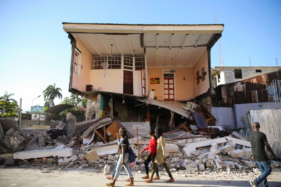 People walk past a home destroyed by the earthquake in Les Cayes, Haiti, Saturday, Aug. 14, 2021. A 7.2 magnitude earthquake struck Haiti on Saturday, with the epicenter about 125 kilometers (78 miles) west of the capital of Port- au-Prince, the US Geological Survey said. (AP Photo/Joseph Odelyn)