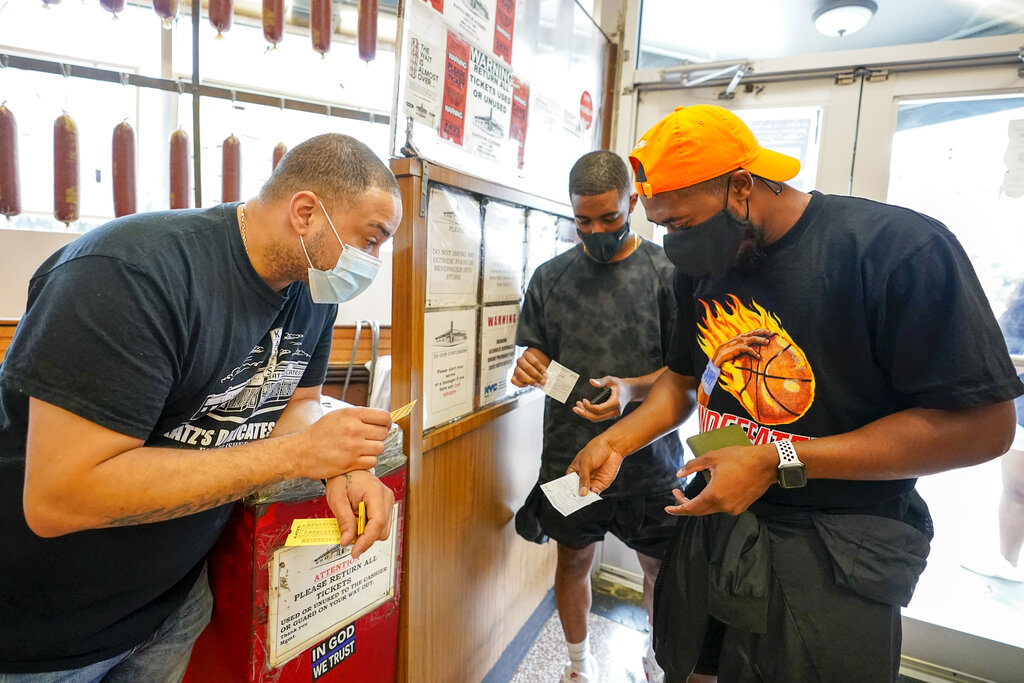 A Katz's Deli employee, left, checks the proof of vaccination from customers who will be eating inside the restaurant, Tuesday, Aug. 17, 2021, in New York. (AP Photo/Mary Altaffer)