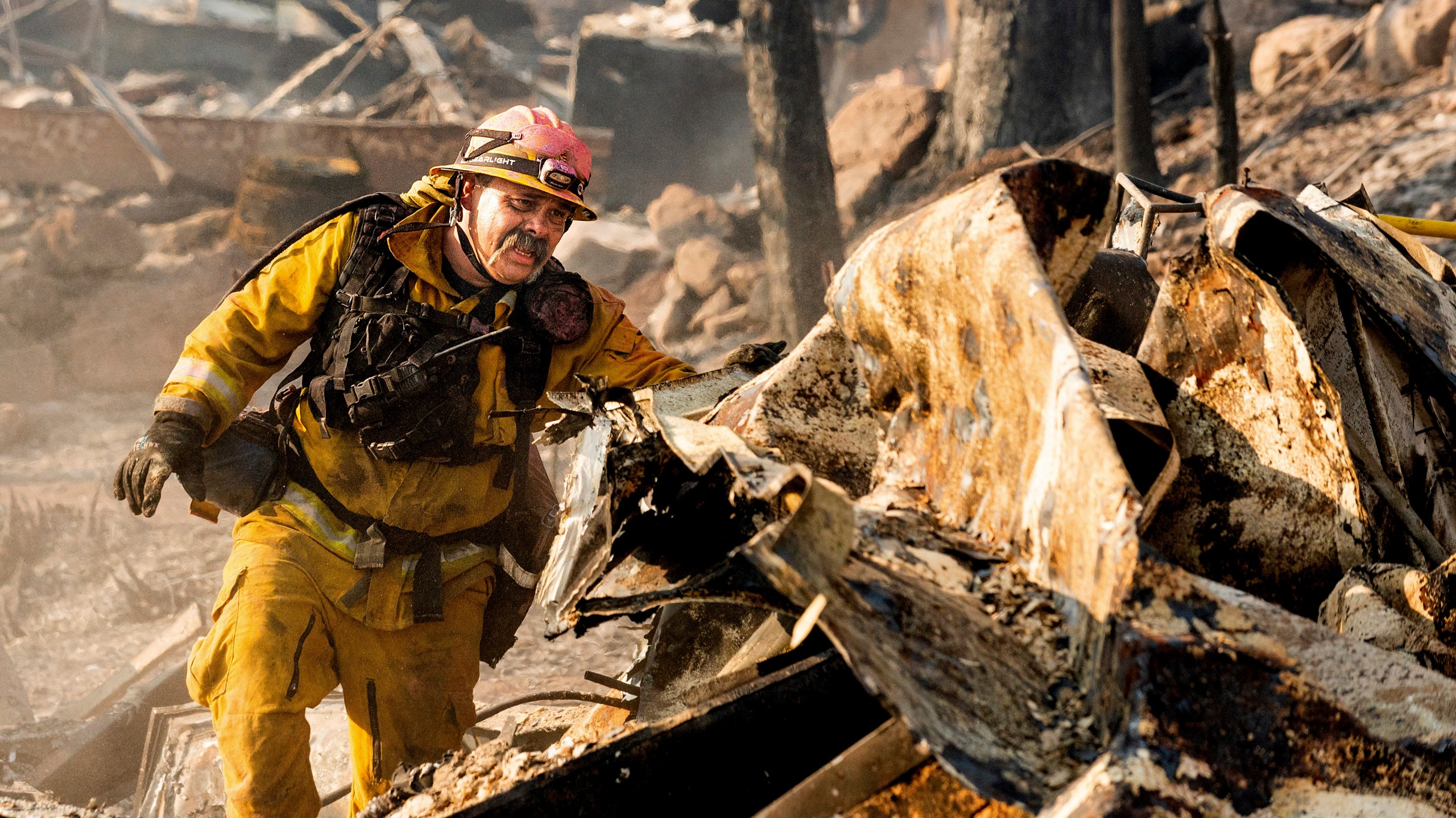 Firefighter Jesse Viescas searches through a residence at Cache Creek Mobile Home Estates where the Cache Fire leveled dozens of homes, Wednesday, Aug. 18, 2021, in Clearlake, Calif. (AP Photo/Noah Berger)