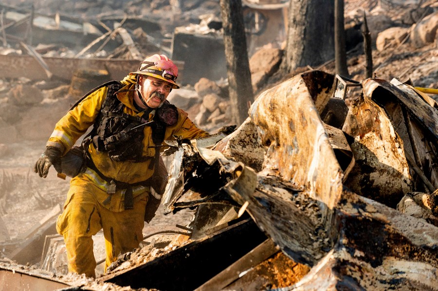 Firefighter Jesse Viescas searches through a residence at Cache Creek Mobile Home Estates where the Cache Fire leveled dozens of homes, Wednesday, Aug. 18, 2021, in Clearlake, Calif. (AP Photo/Noah Berger)