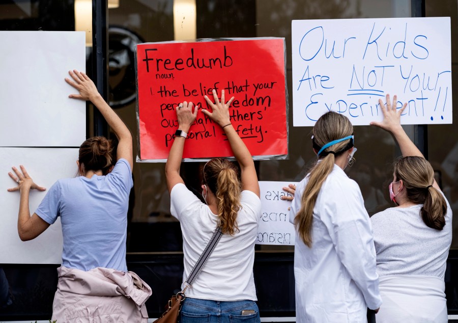 People in favor of a mask mandate for Cobb County schools hold signs against the window to the office during the school board meeting Thursday, Aug. 19, 2021, in Marietta, Ga. (Ben Gray/Atlanta Journal-Constitution via AP)